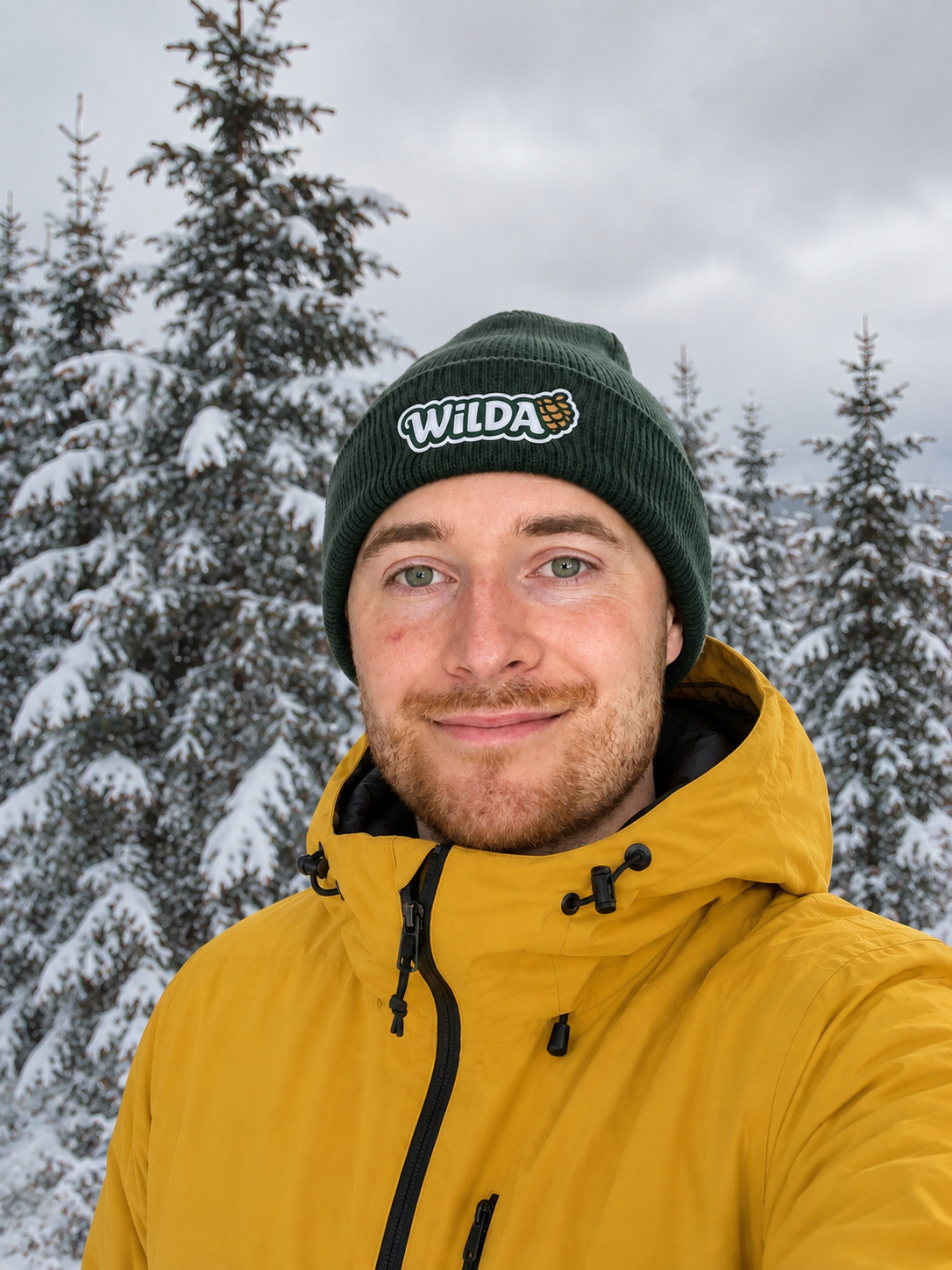 Daniel Nagy, founder of Wilda, in a green Wilda beanie among snowy spruce trees